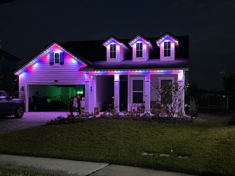 Trim lighting enhances the house's exterior with vibrant colors against a dark evening sky