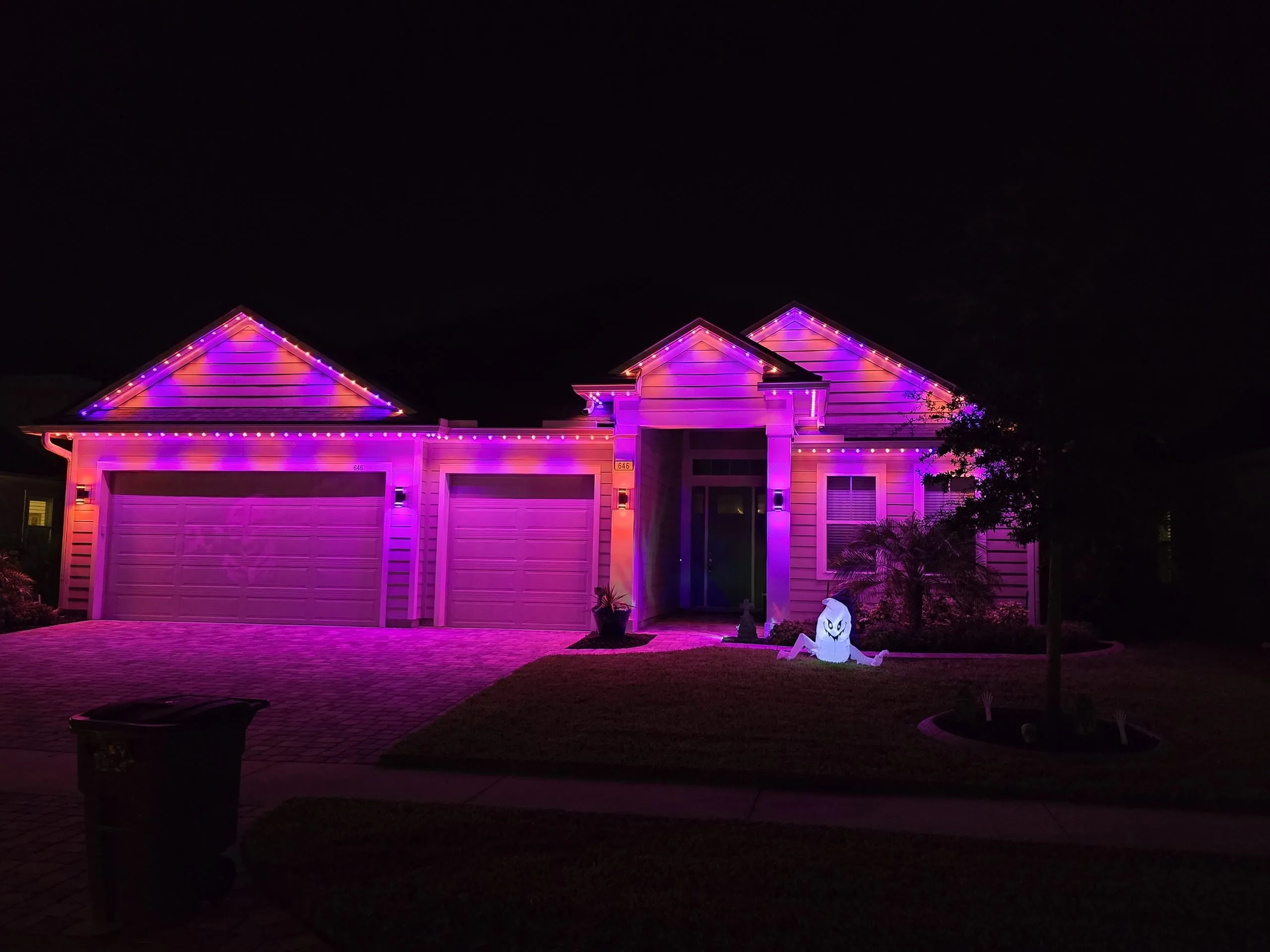 A house is brightly illuminated with purple lights and a ghost decoration in the yard