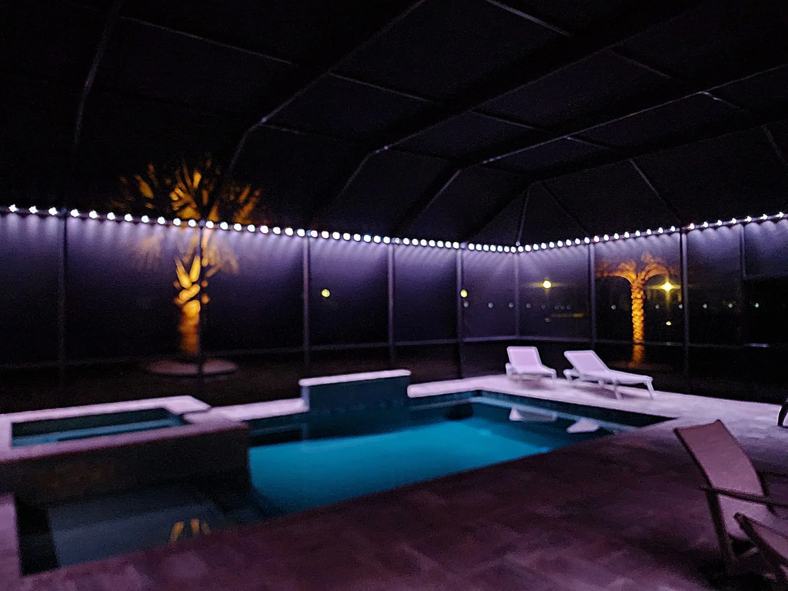 A serene pool area glows with purple lights under a starlit night sky